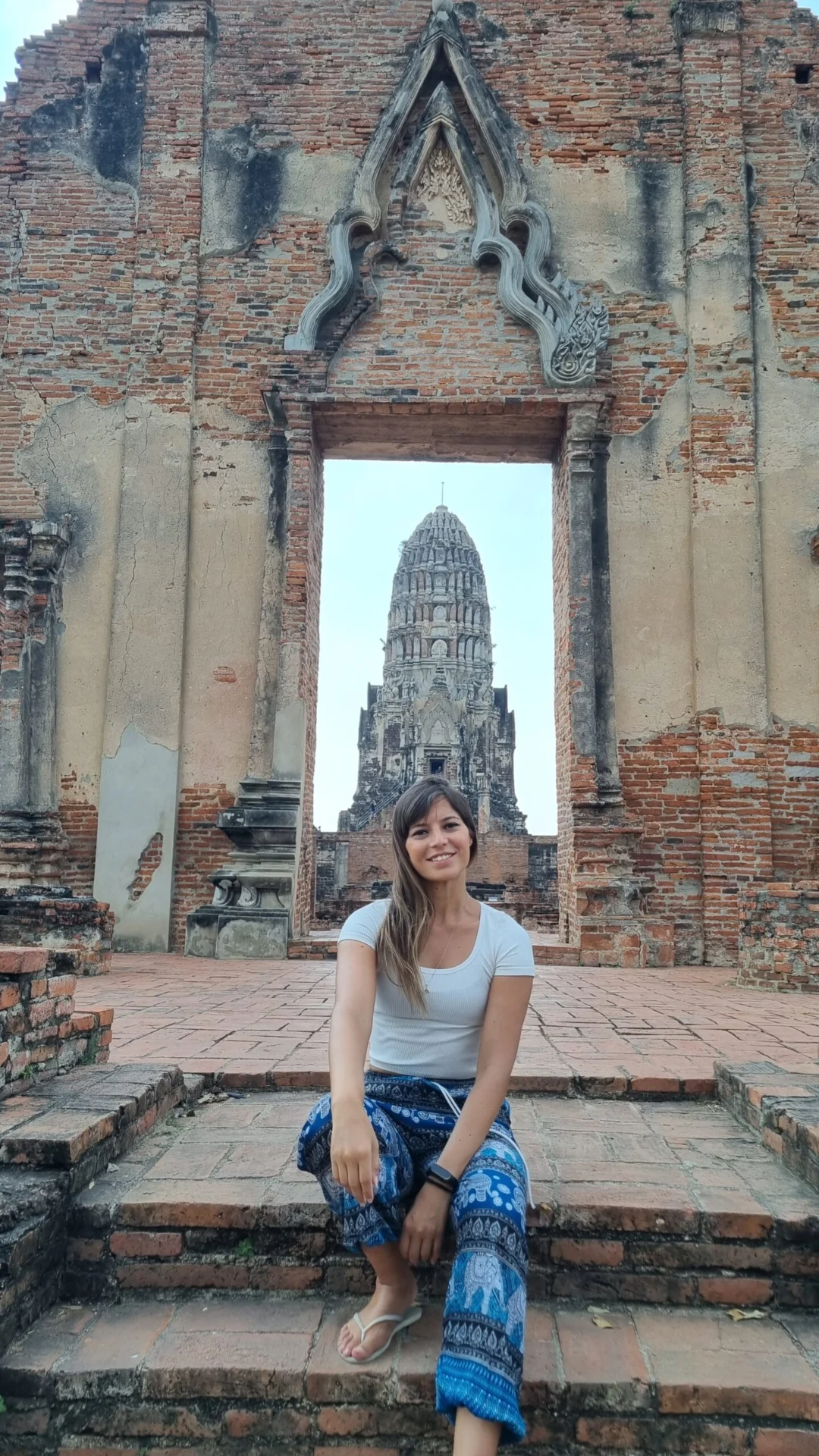 A woman sits in a brick temple doorway with a tall ruin framed in the background.