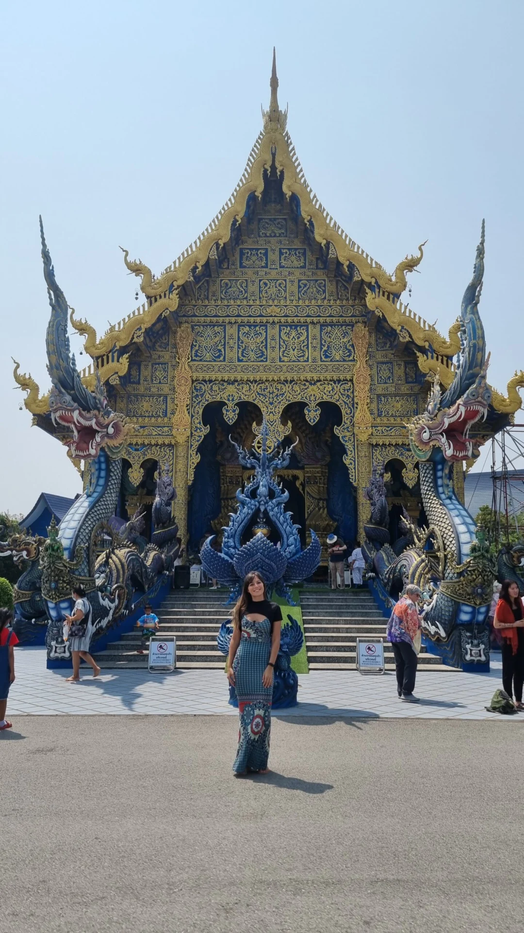Woman standing in front of an ornate blue and gold temple façade with dragon details.