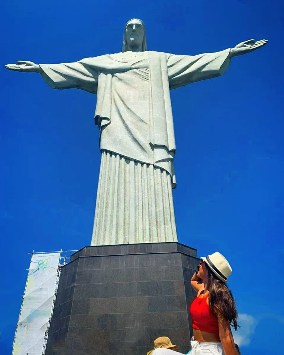 Woman in a red top and hat looking up at a large Christ the Redeemer statue