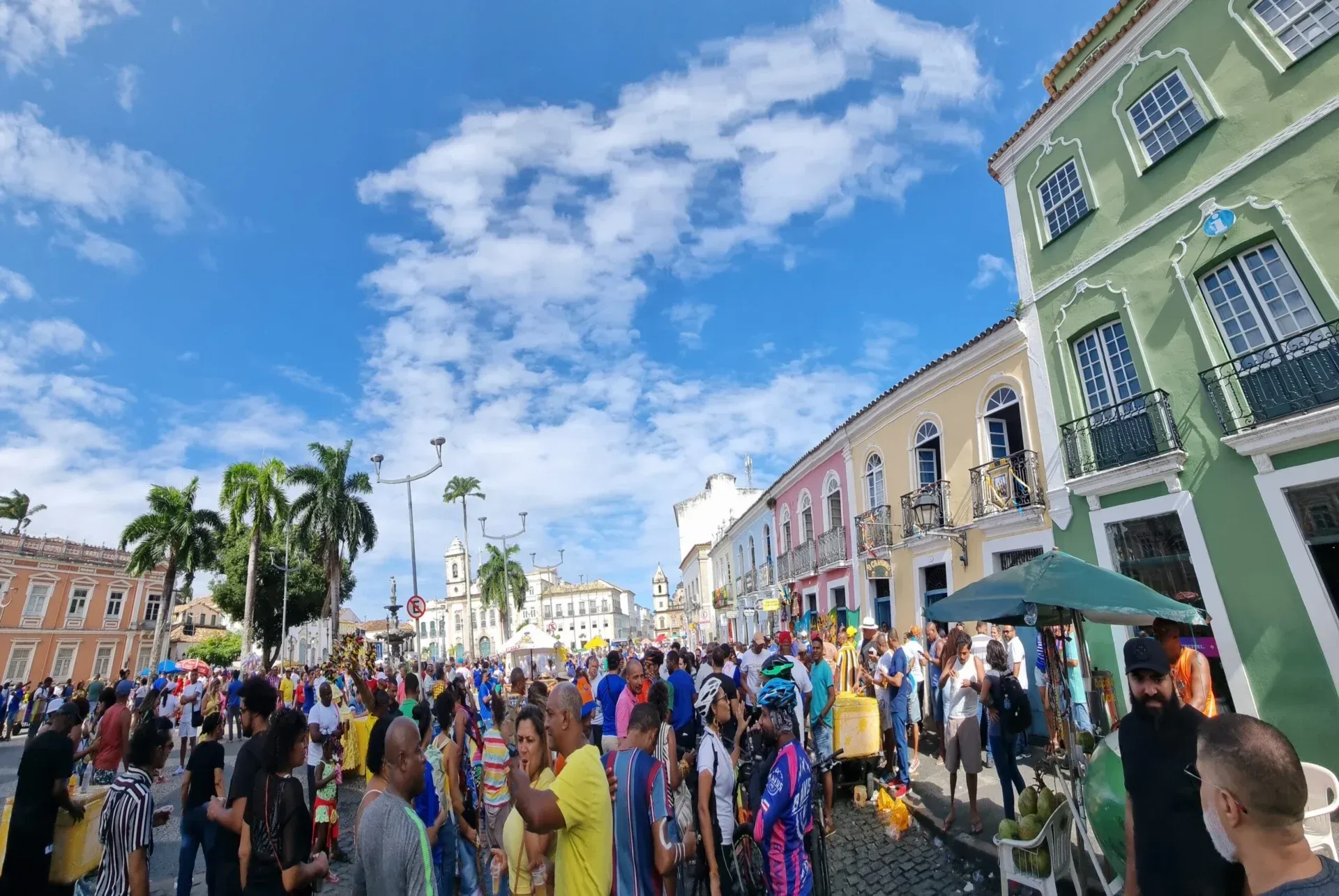 Crowded square with colorful colonial buildings and palm trees under a bright blue sky