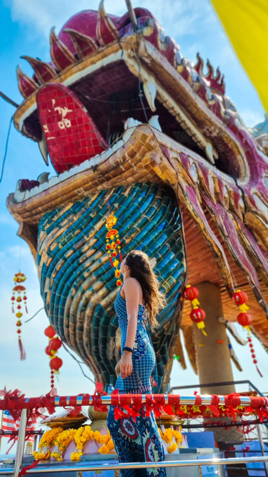 A woman stands below a giant dragon-shaped temple tower decorated with red lanterns.