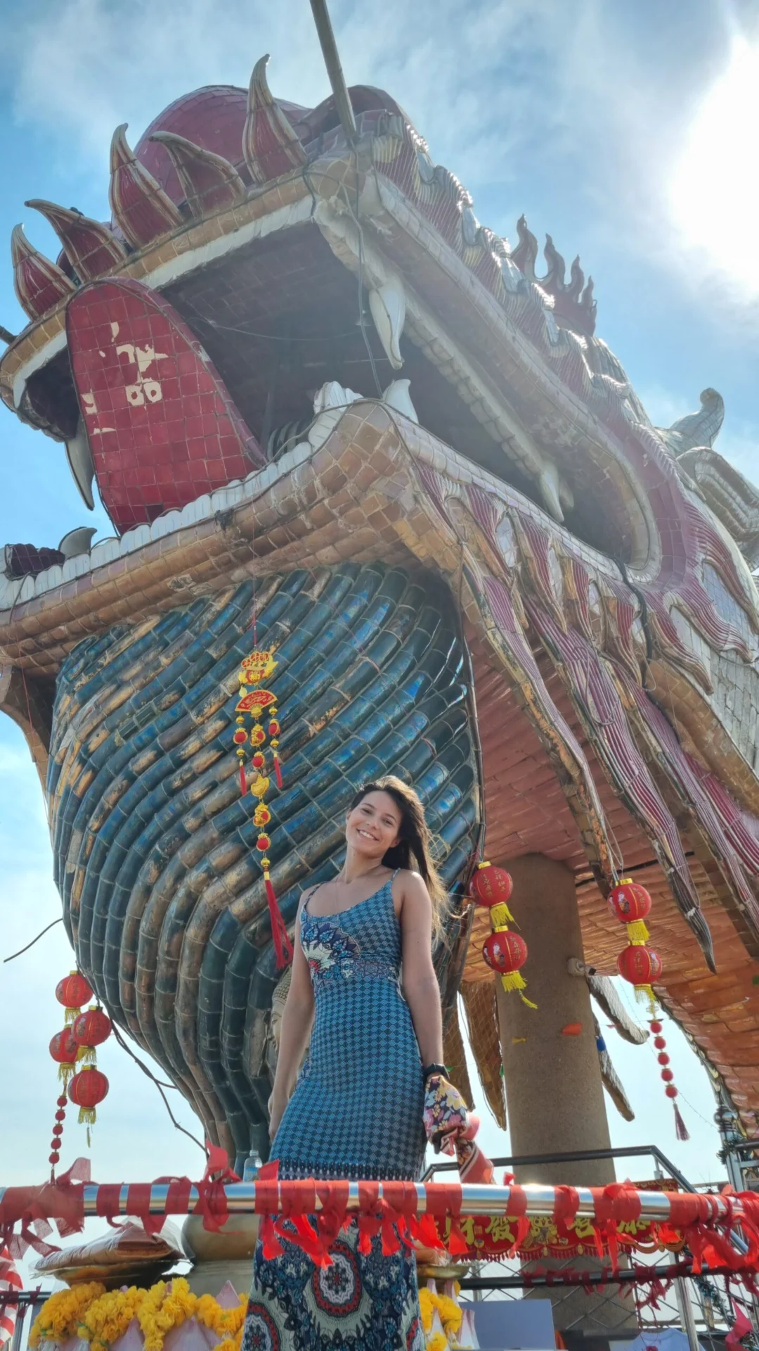 A woman posing beneath the dragon temple tower with sunlight overhead.