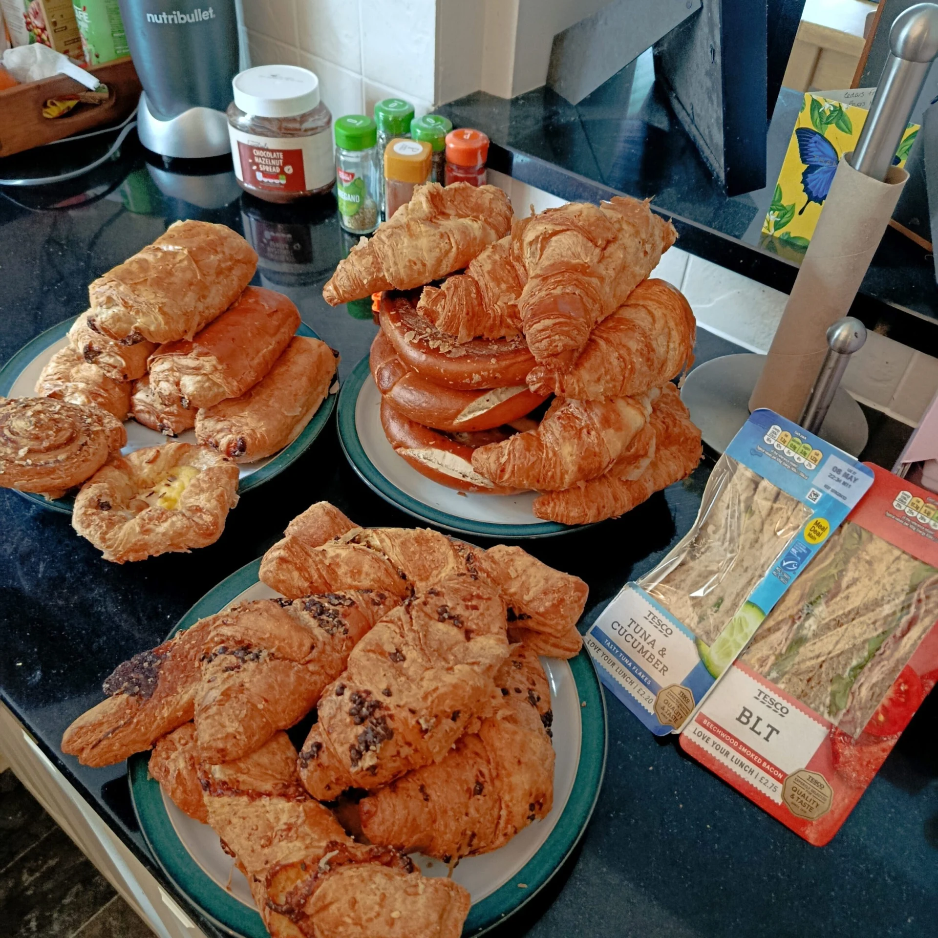 Several plates of pastries and sandwiches are laid out on a kitchen counter.