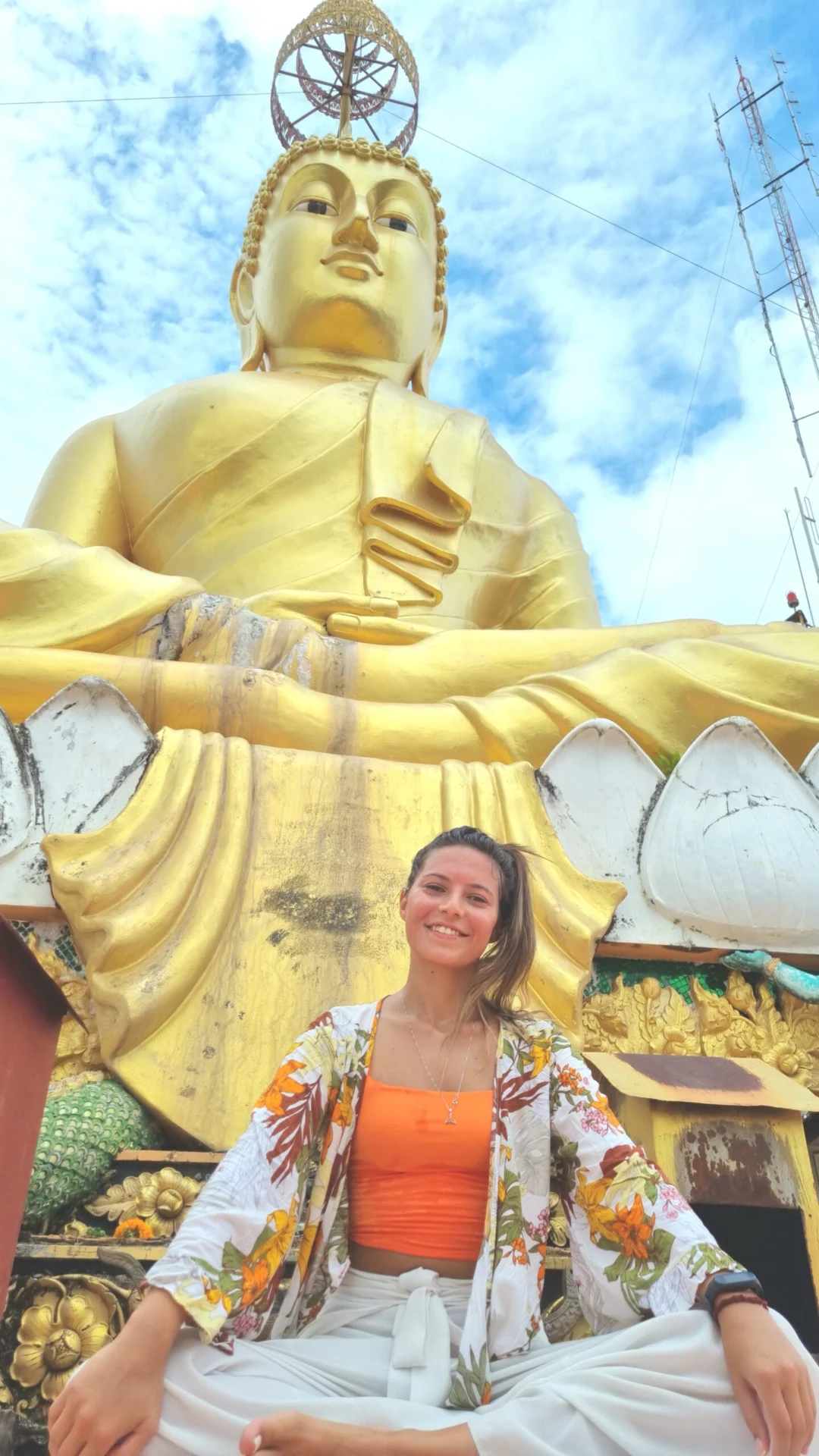 A large golden Buddha statue with a visitor seated in front.