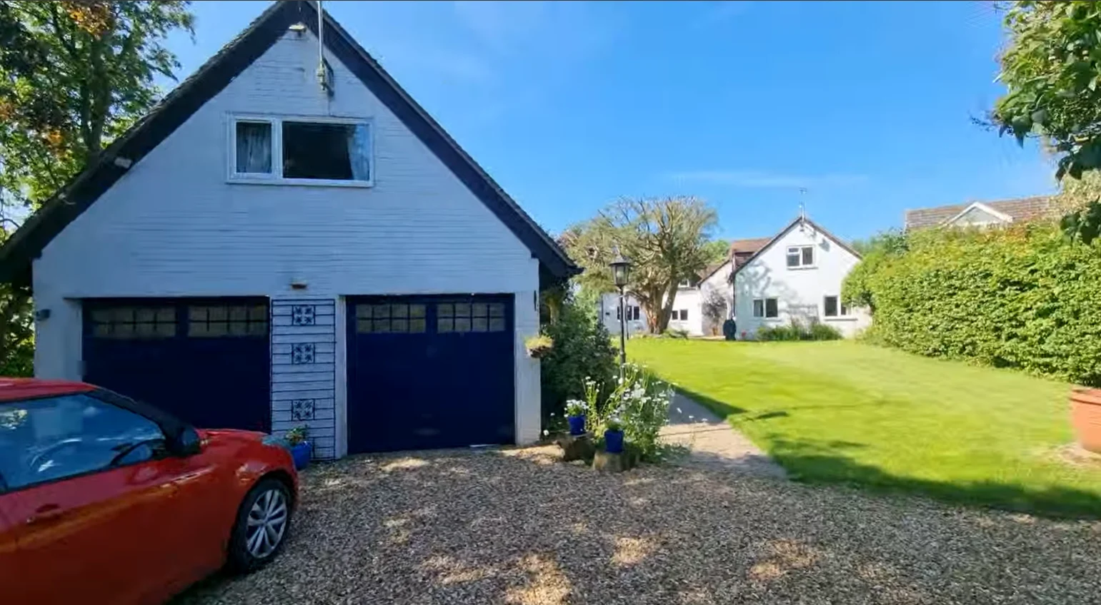 A white house with a driveway and a red car parked outside on a sunny day.