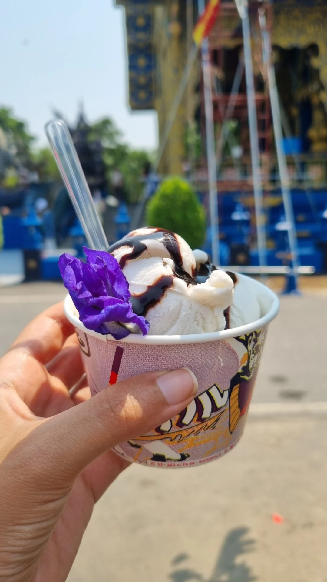 Hand holding a cup of ice cream with a temple blurred in the background.