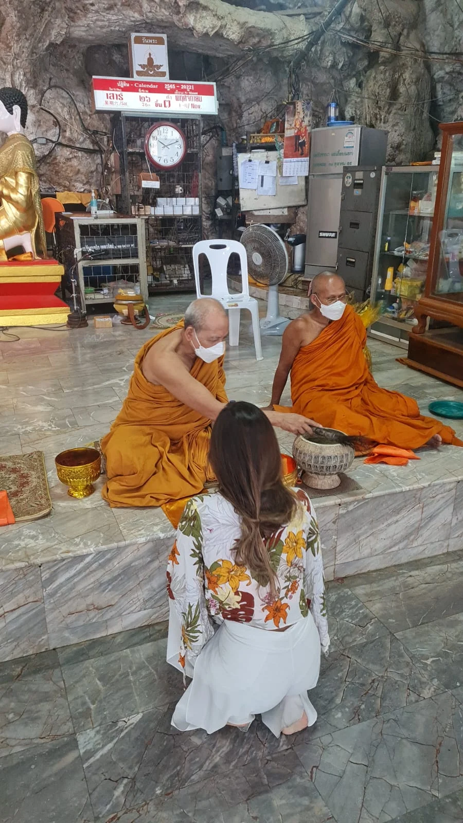 Two monks in orange robes giving a blessing inside a temple hall.