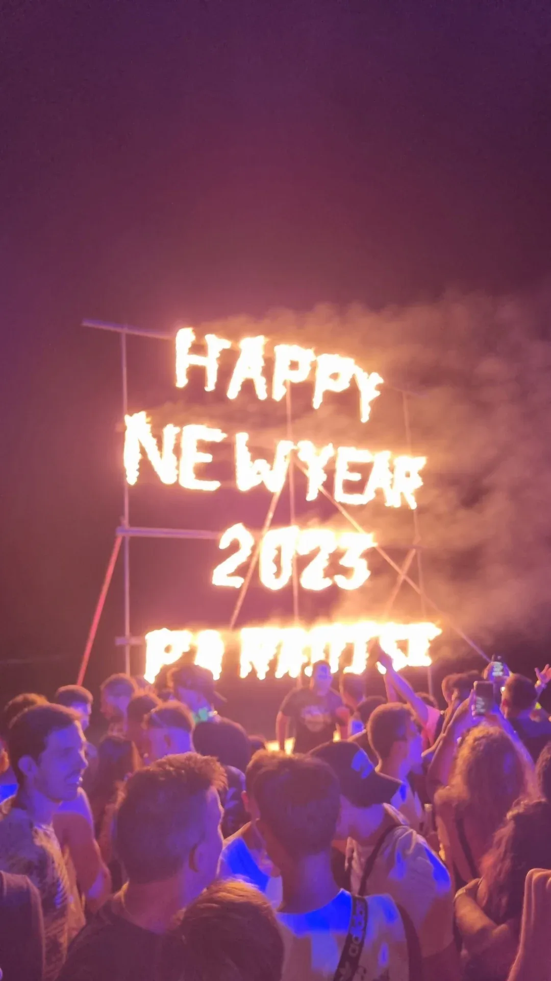 Crowd watching a fiery New Year sign at a nighttime party.