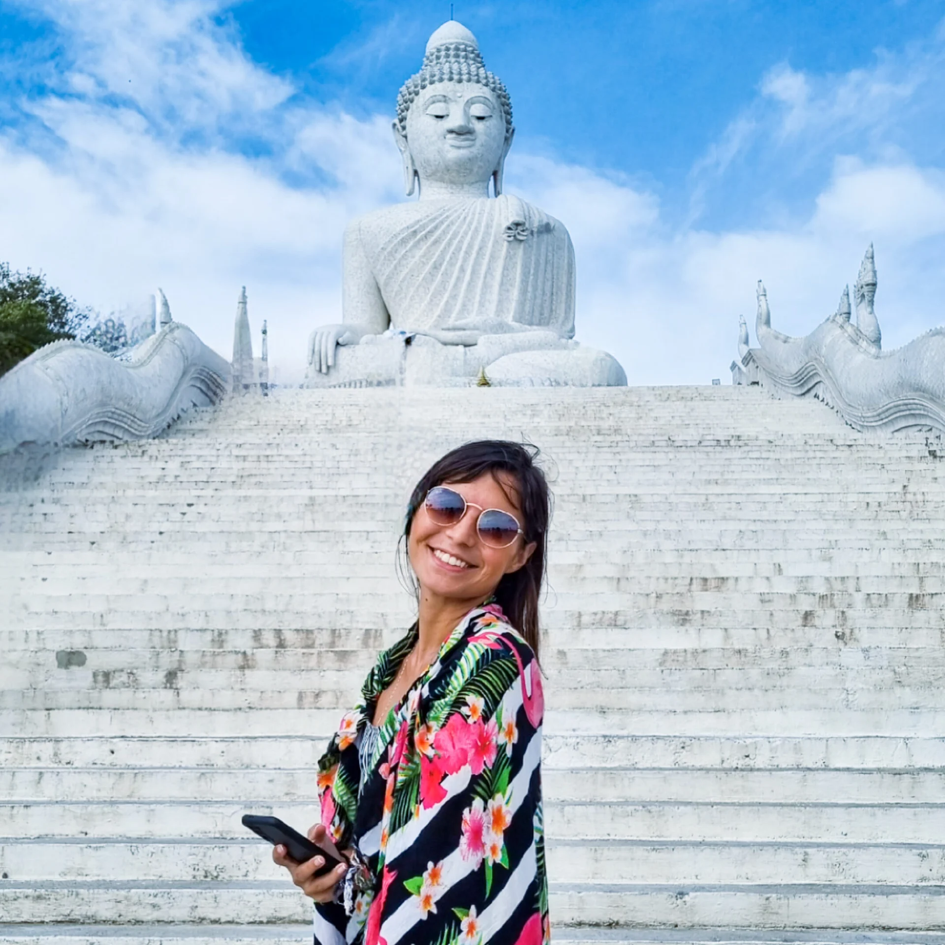 Woman standing on the steps in front of a large white Buddha statue on a hill