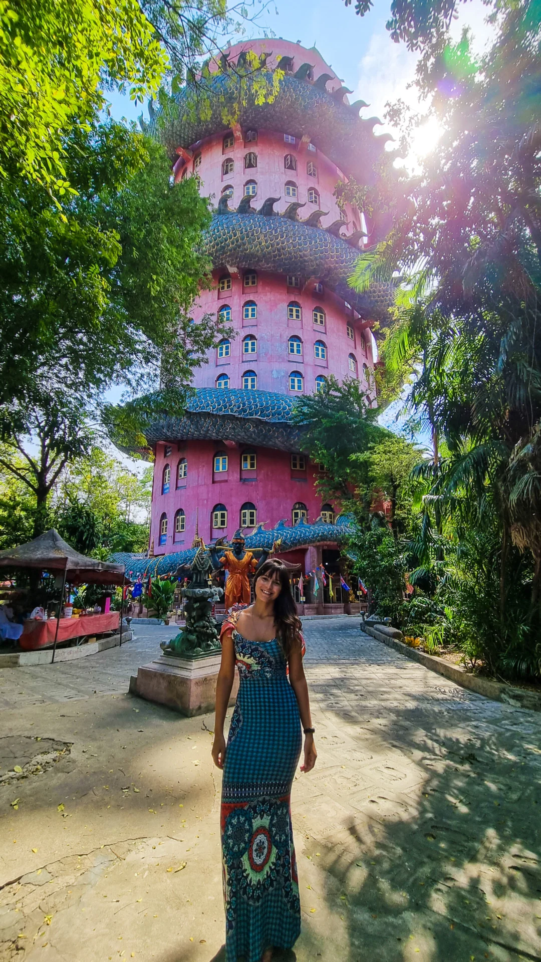 A tall pink temple tower rises above a garden path surrounded by dense greenery.