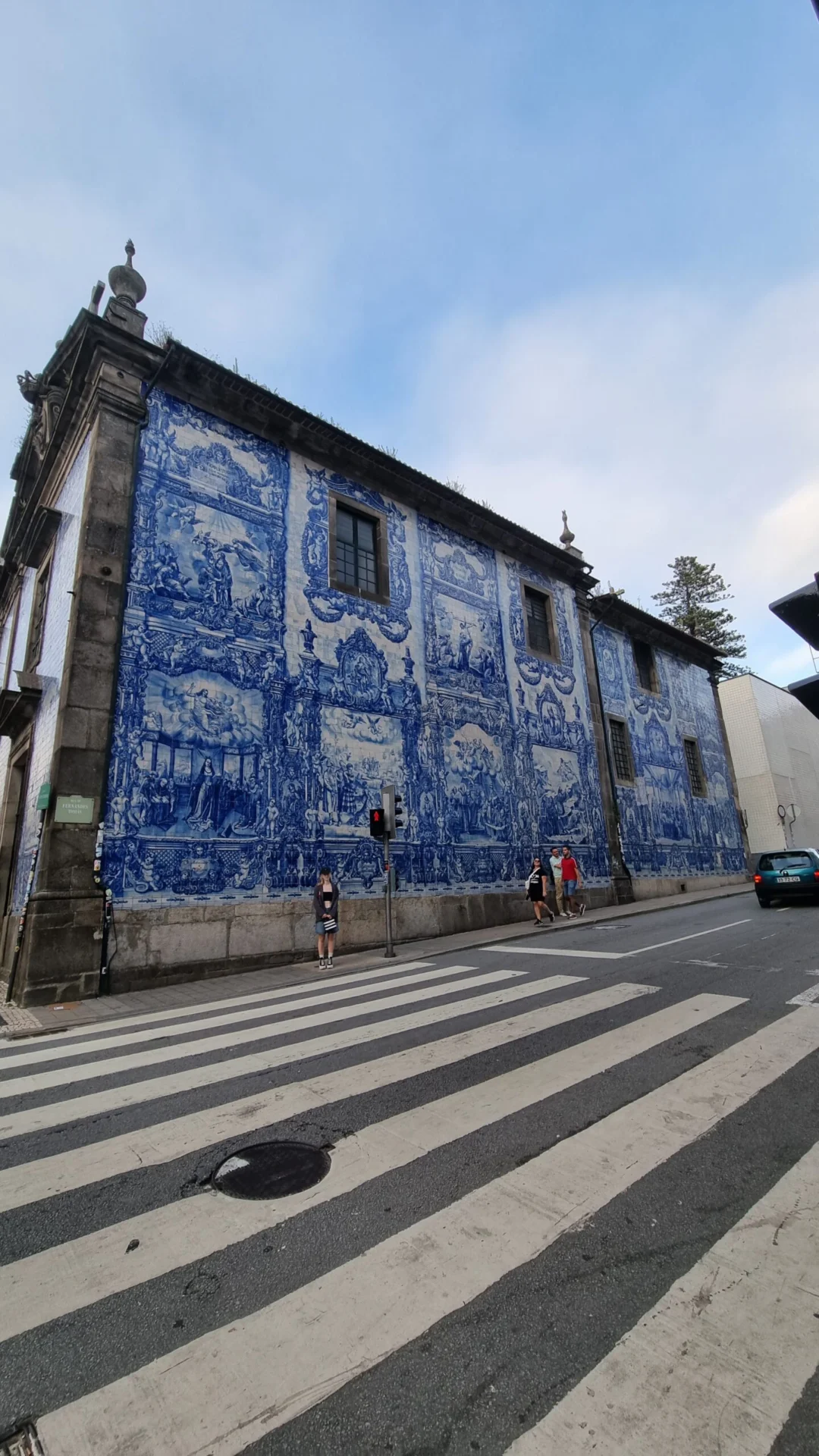 Large building covered in blue tile murals beside a crosswalk on a city street.