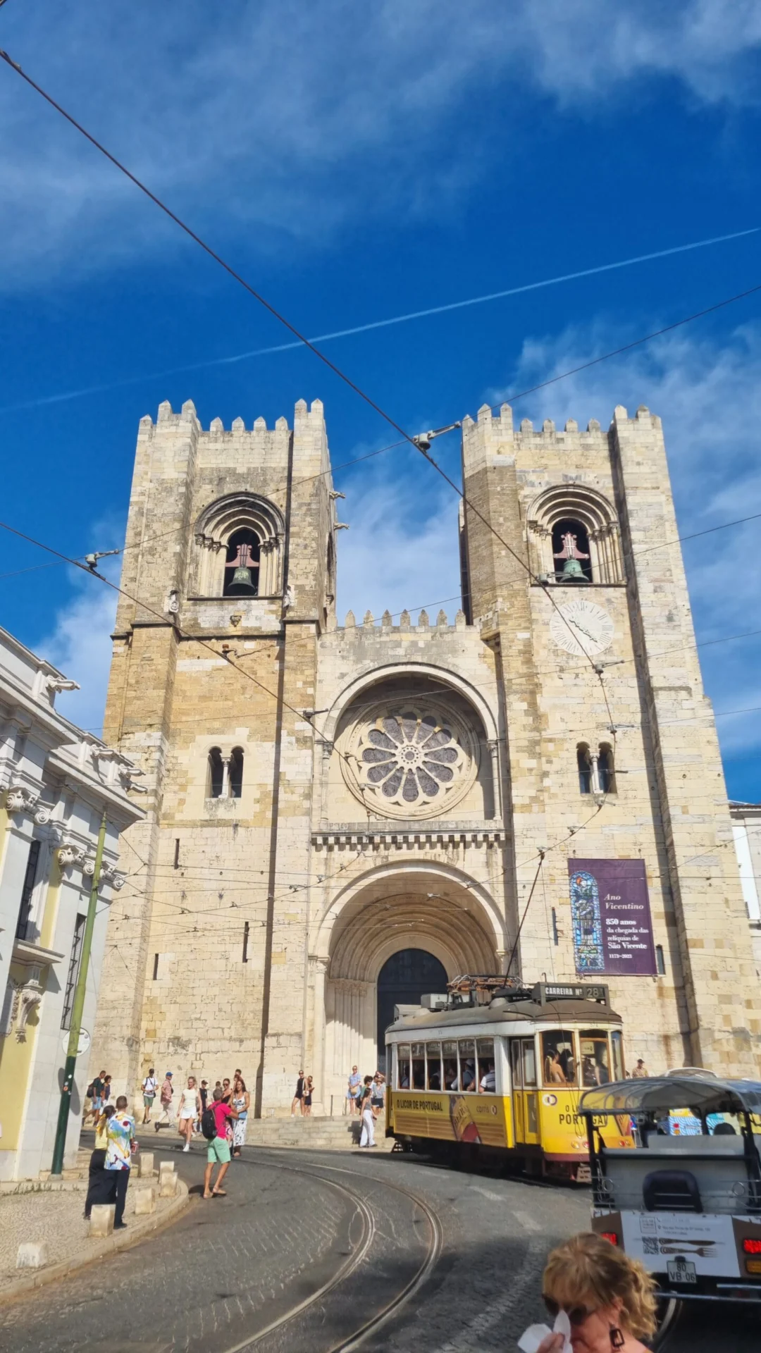 A cathedral facade with twin towers overlooks a steep Porto street with a yellow tram and pedestrians.