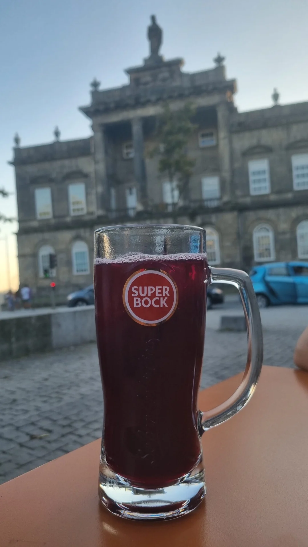 A glass of dark beer on a table with a historic building in the background.