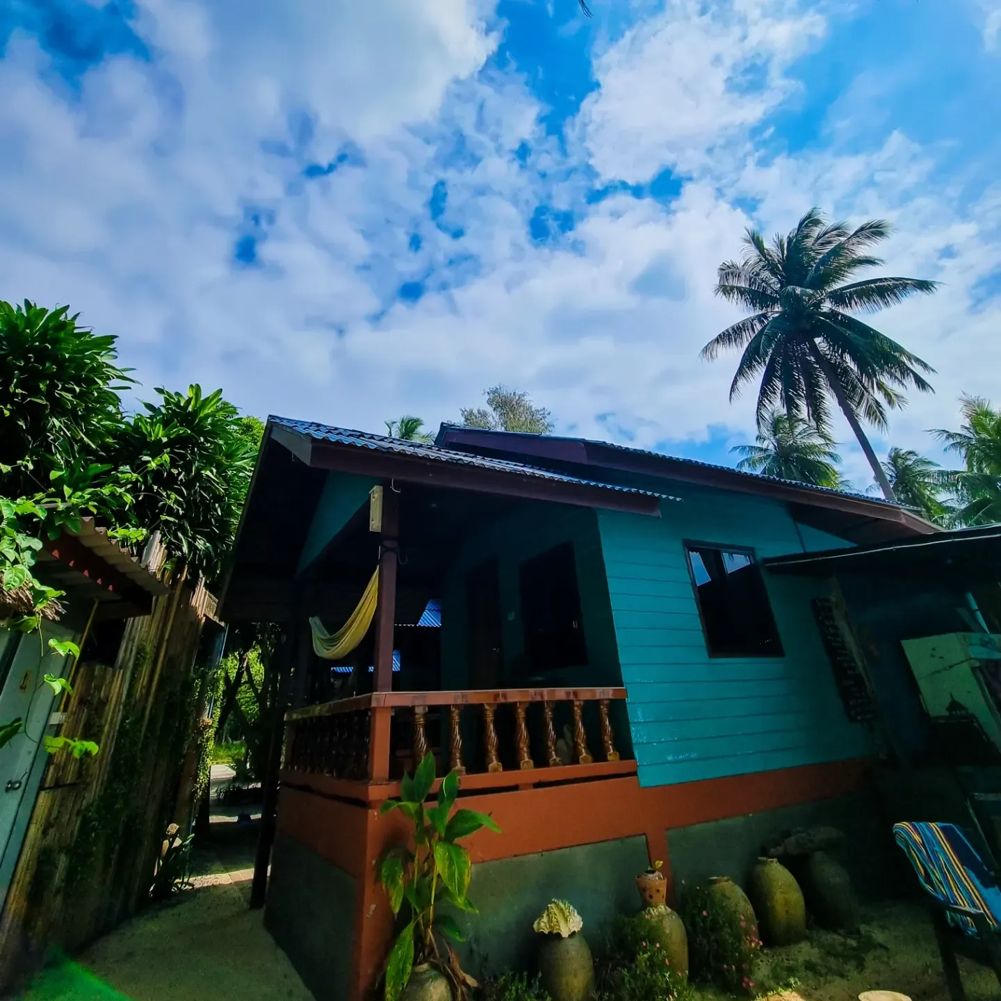 Colorful rustic bungalow with palm trees and a tropical sky overhead.