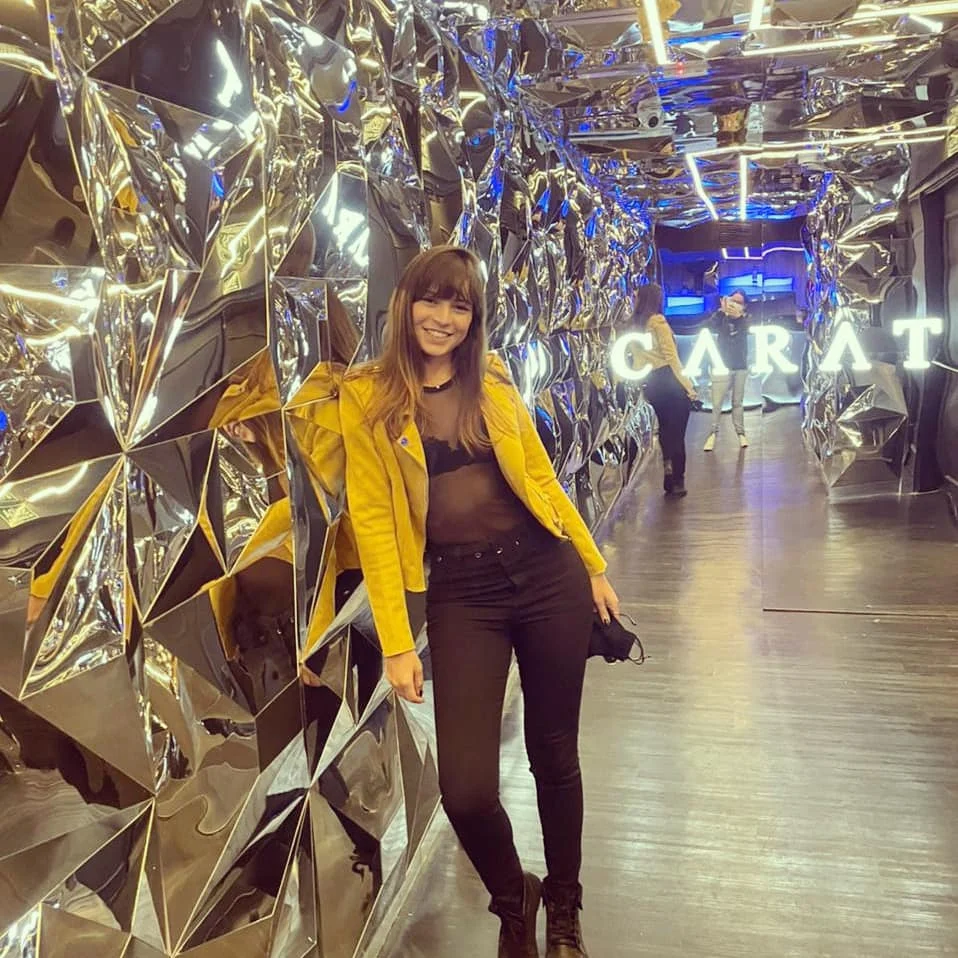Woman standing in a mirrored hallway with bright signage and metallic wall decor.