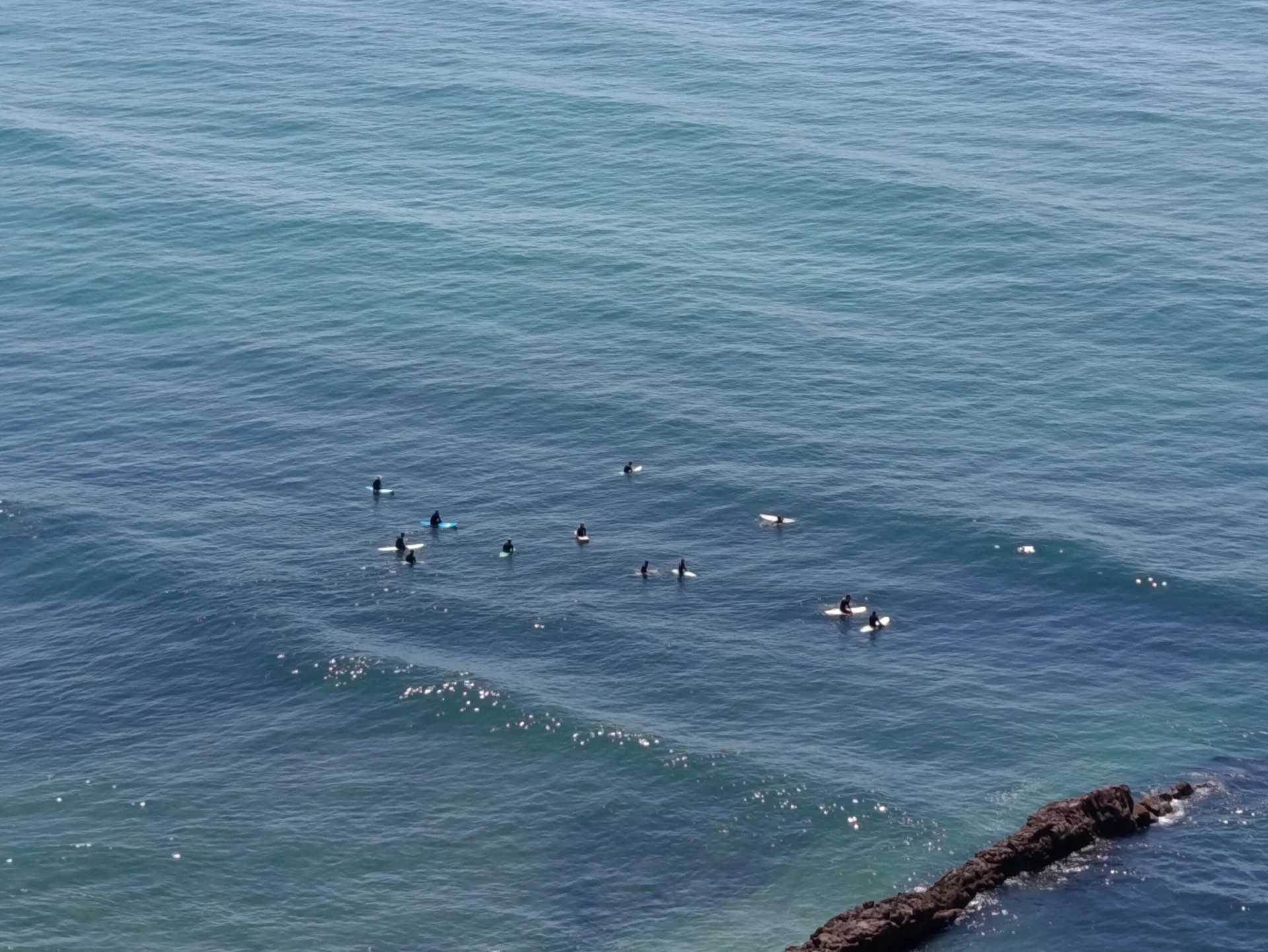 Surfers floating in the ocean near a rocky section of coastline.