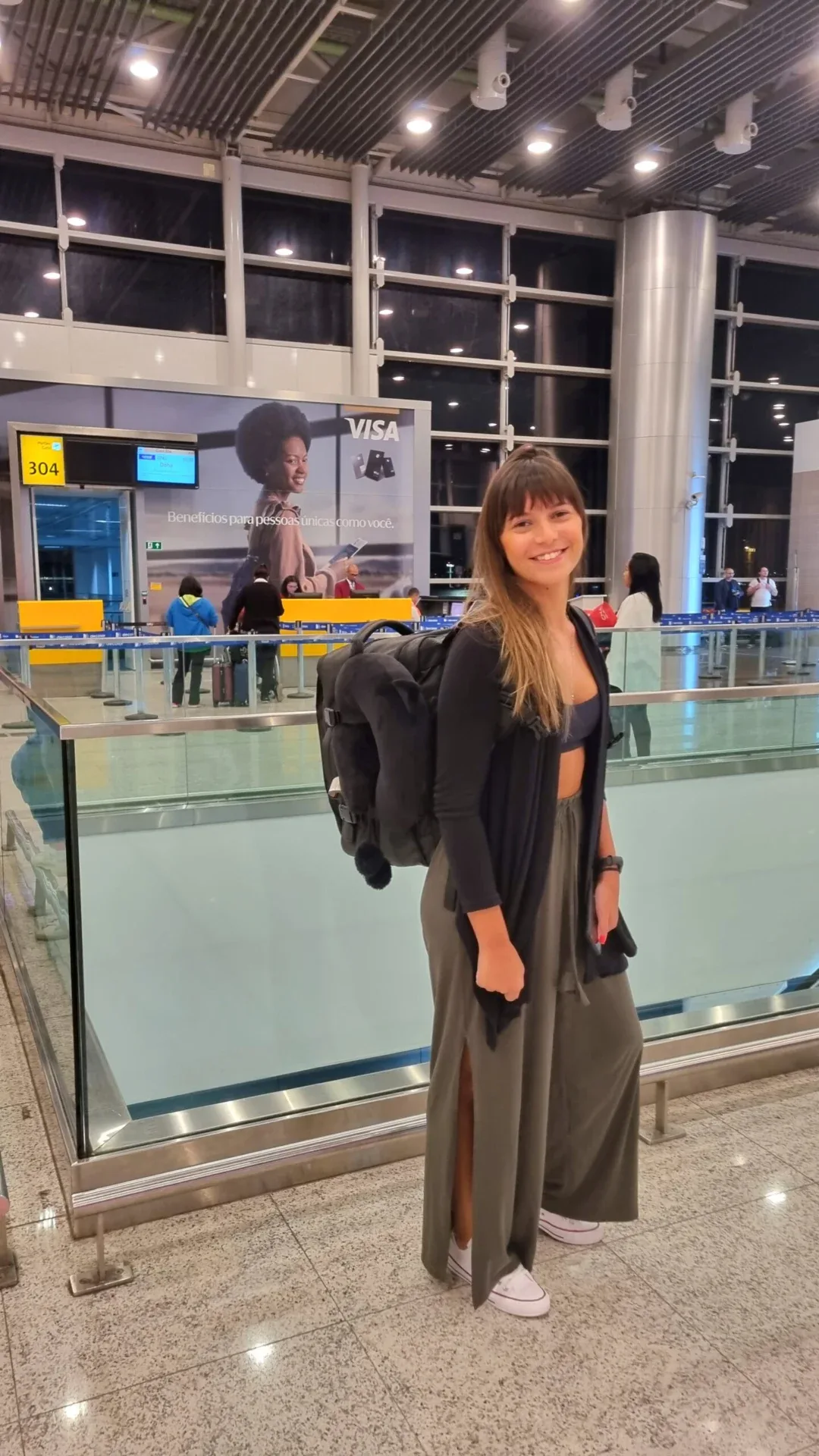 Smiling woman standing with a backpack in an airport terminal.