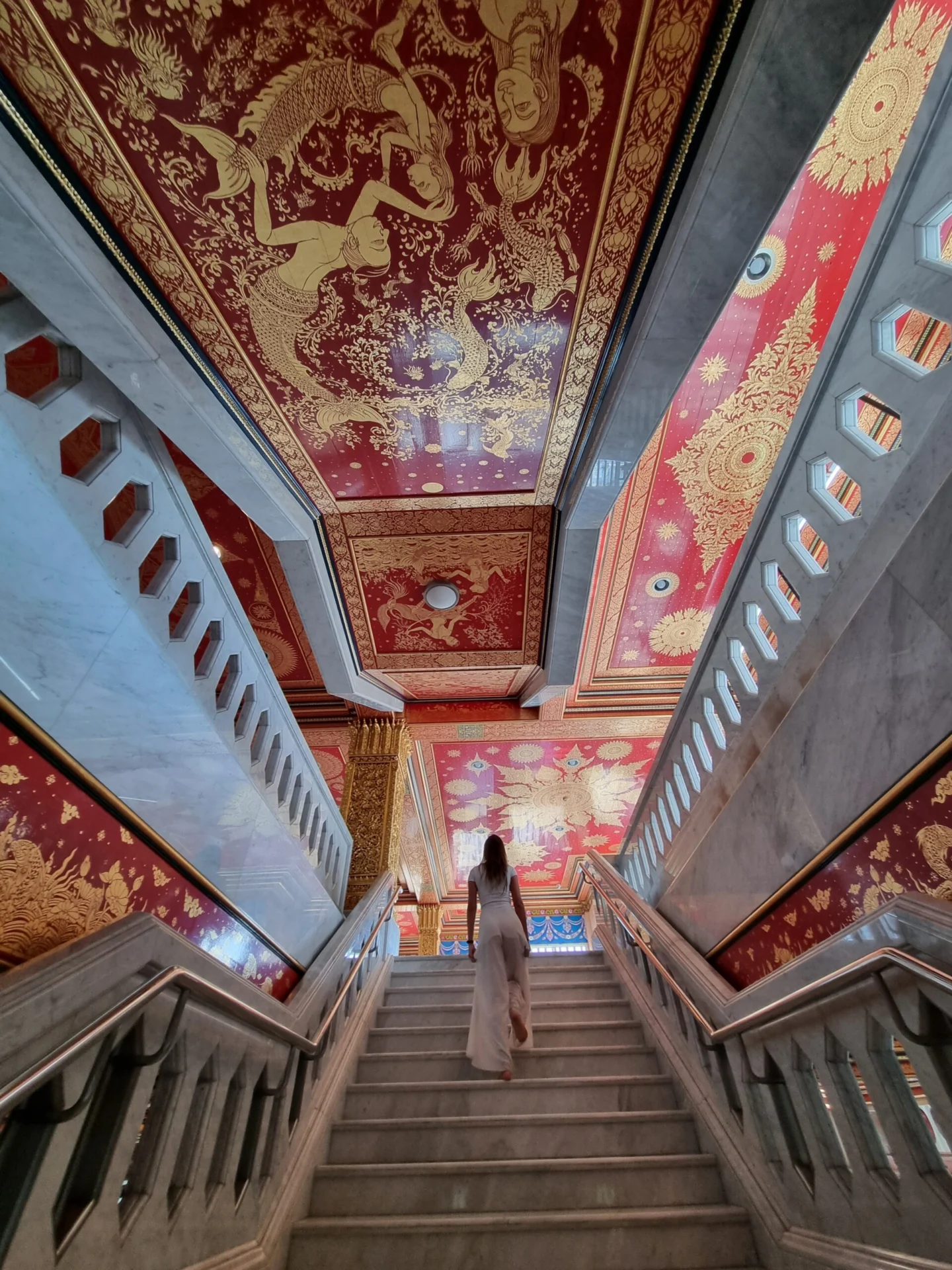 Staircase inside Wat Paknam with ornate red-and-gold ceiling murals and a person walking up