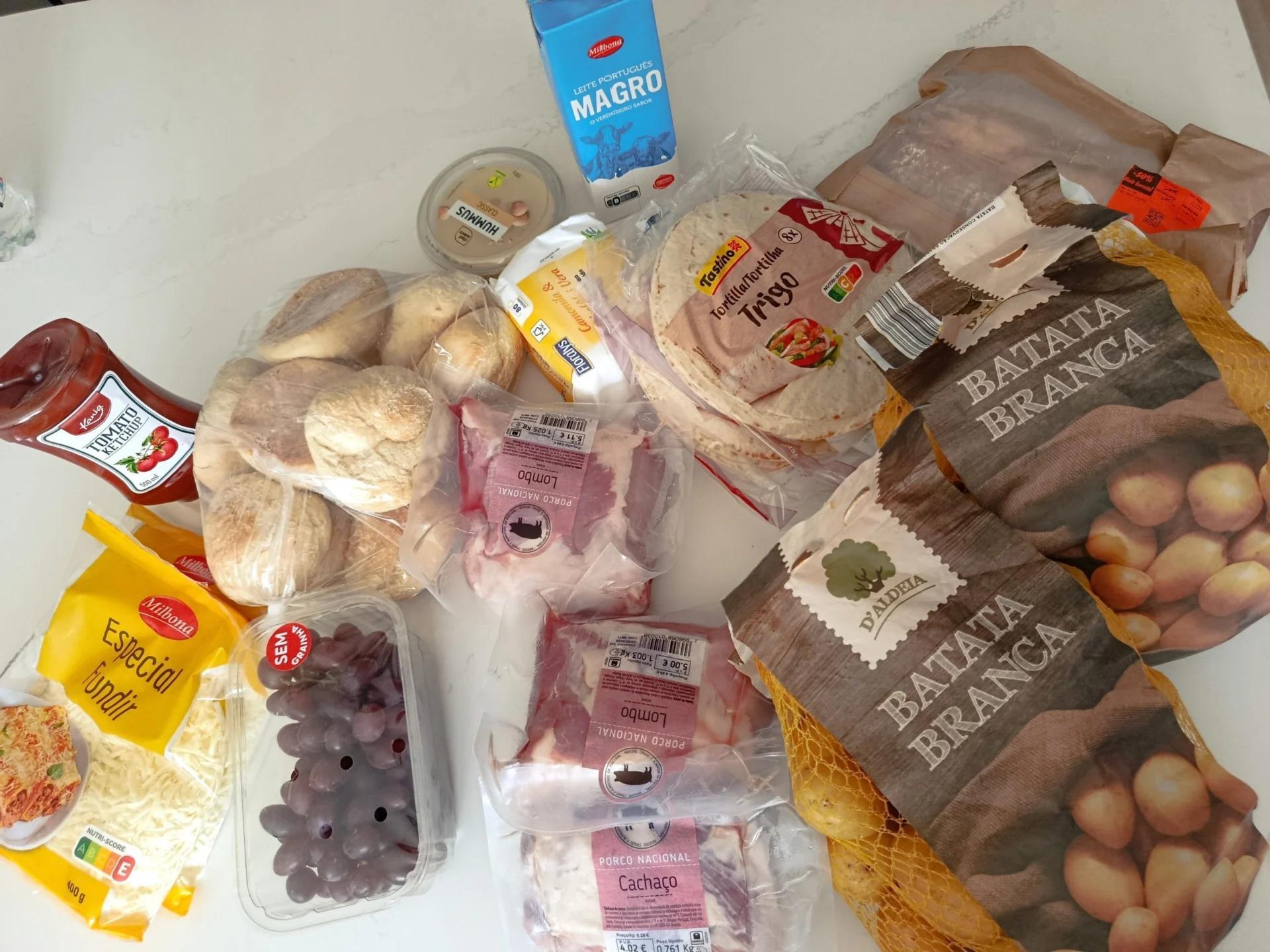 Groceries for a weekly shop laid out on a table, including produce, tortillas, potatoes and dairy.
