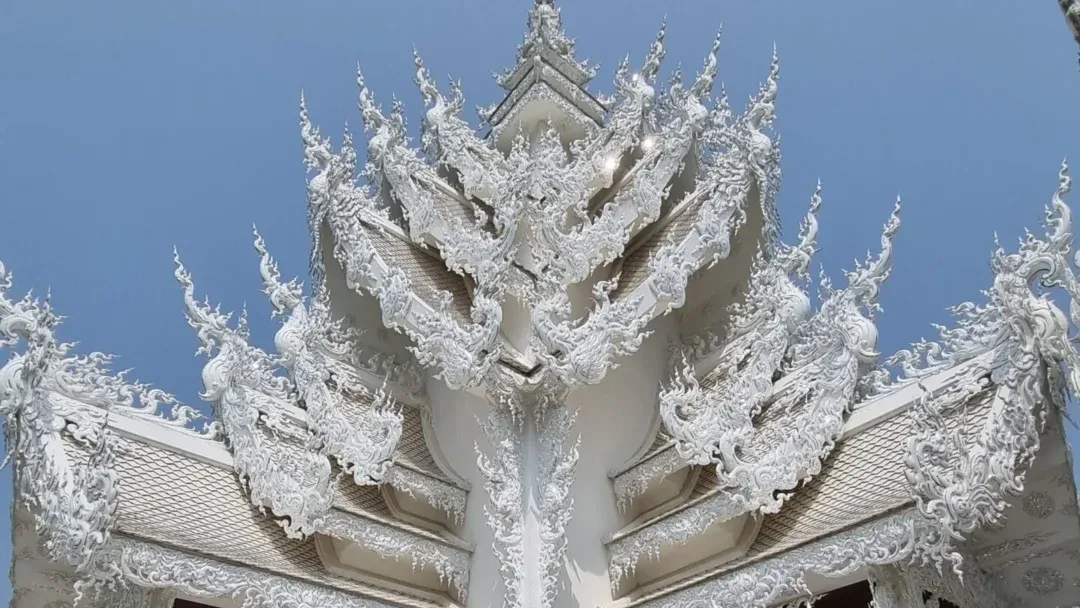 Ornate white gable detail of Wat Rong Khun against a blue sky.