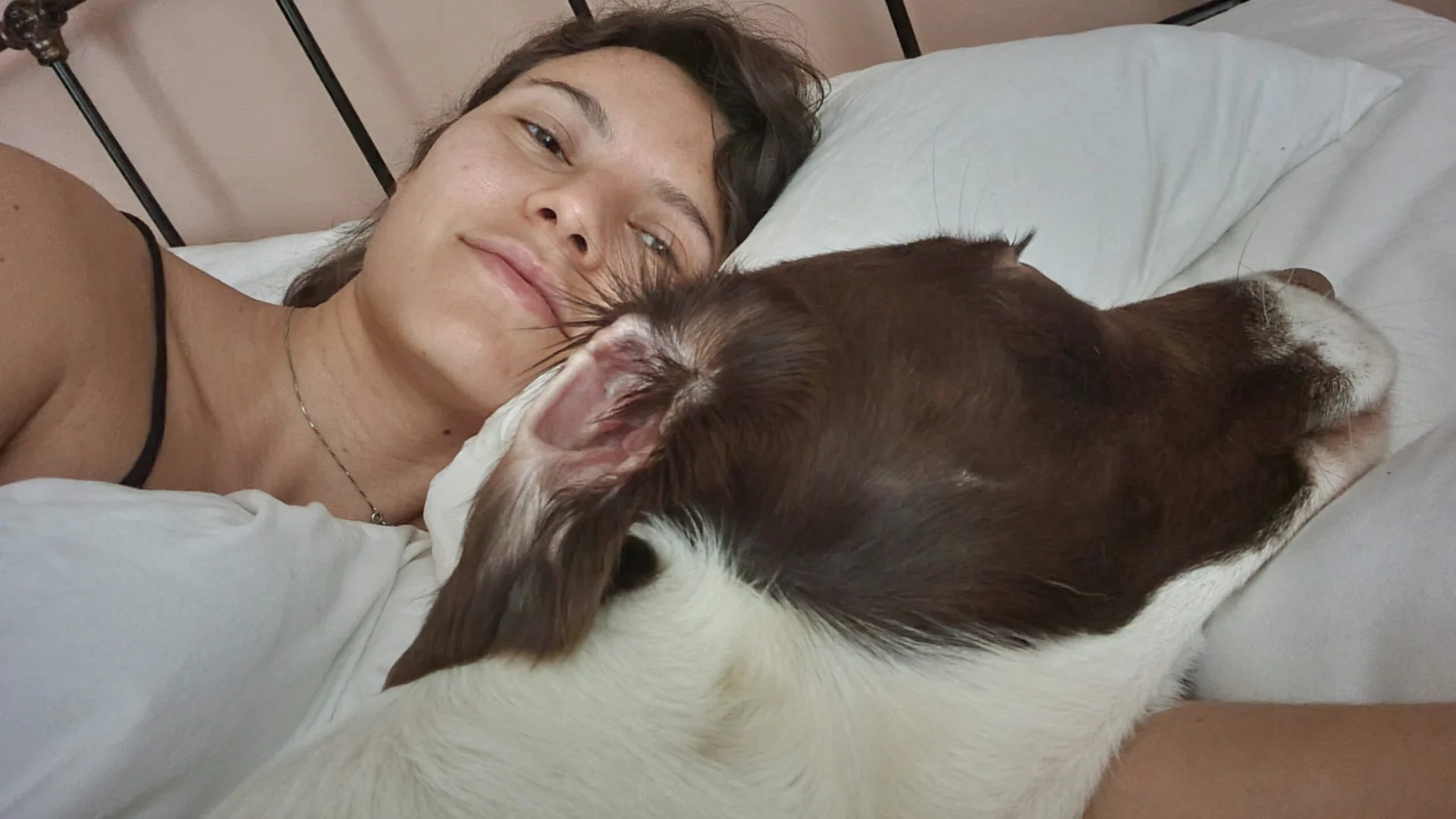 Woman lying in bed with a dog resting against her face and shoulder.