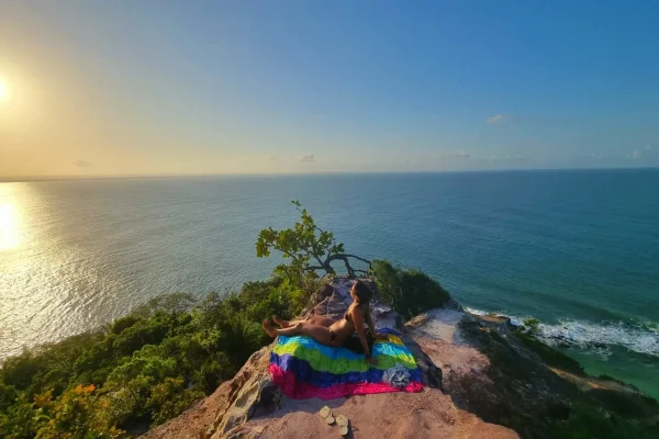 Person relaxing on a rocky viewpoint above the ocean at sunset.