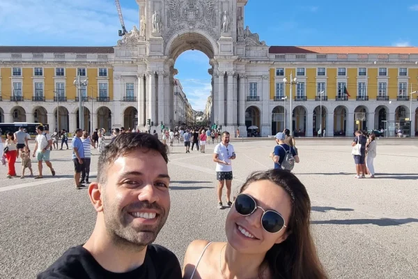 A couple posing for a selfie in front of a large historic arch and square.