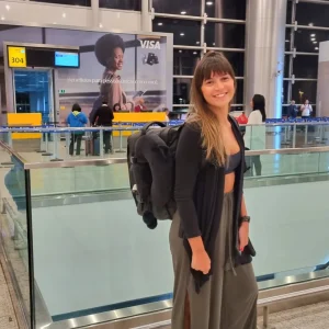 Smiling woman standing with a backpack in an airport terminal.
